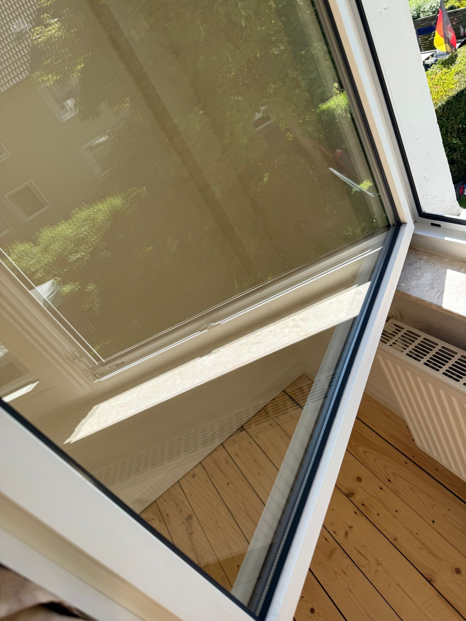 Ein geöffnetes Fenster mit Blick auf grüne Büsche und ein deutsches Fähnchen im Garten