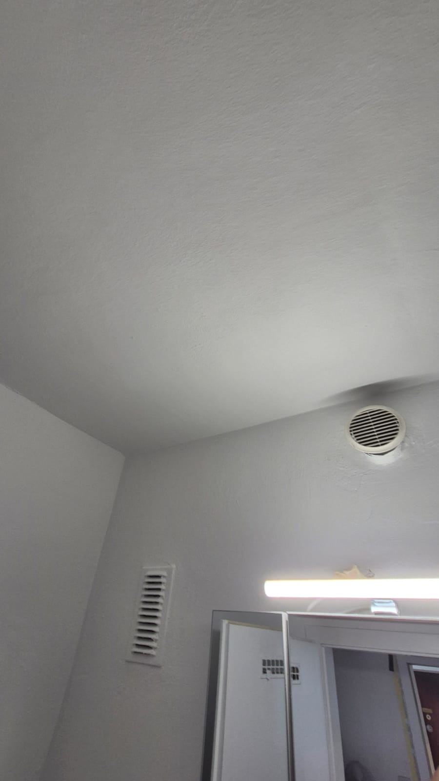 Weisse Badezimmerdecke mit zwei Lüftungsgittern und einem Spiegel mit Licht