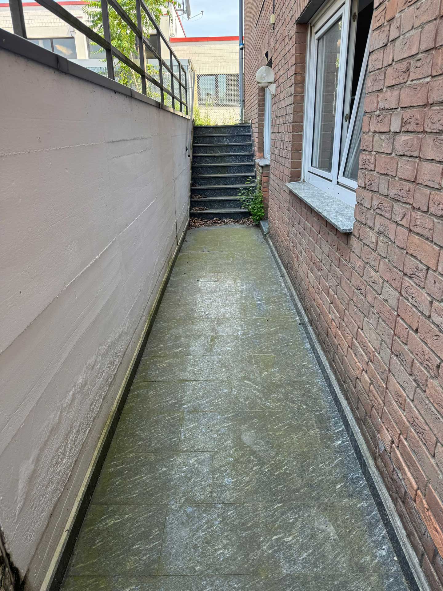 Ein schmaler gepflasterter Durchgang mit moosigem Boden, Treppen und Backsteinwand