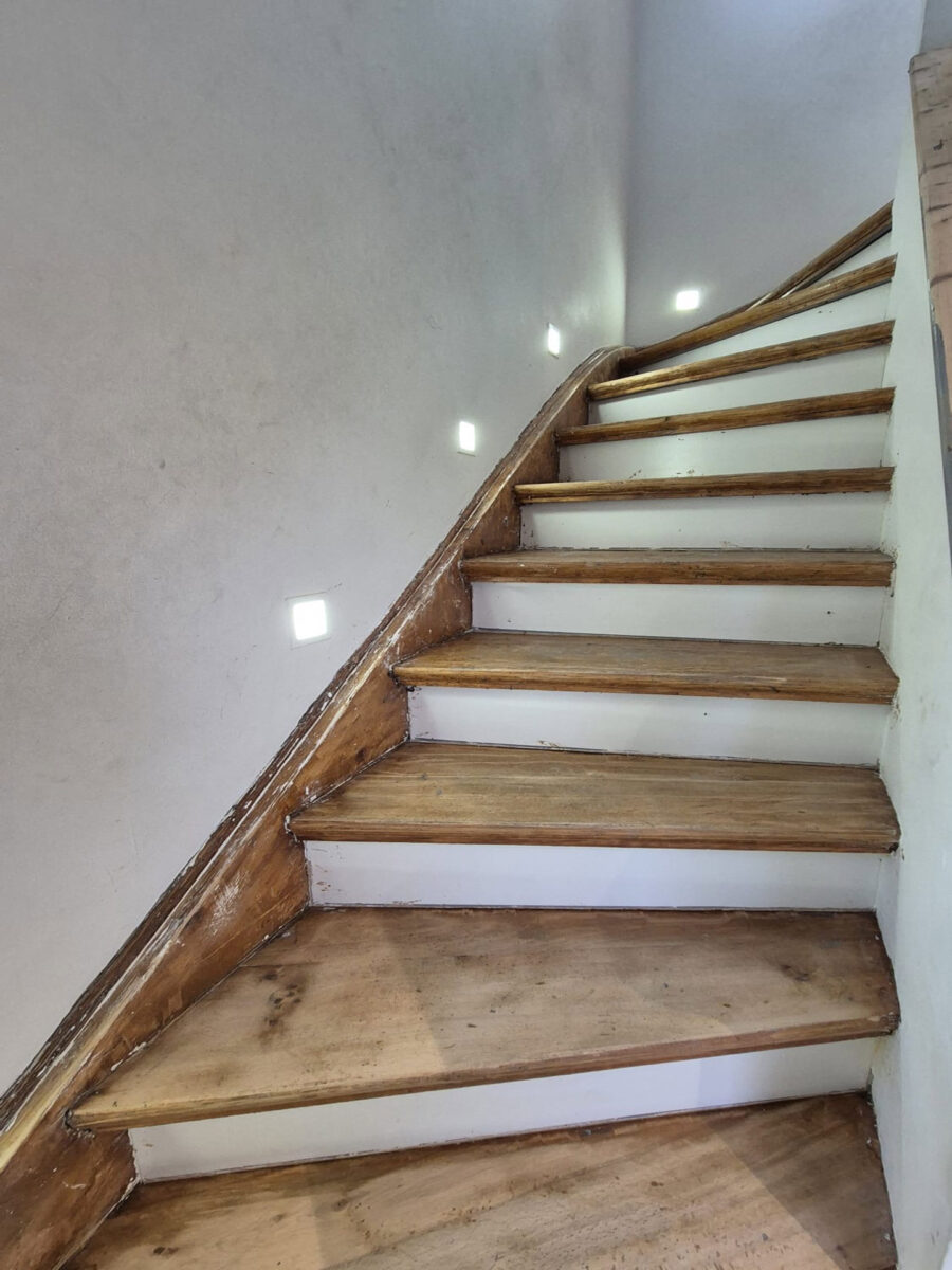 Eine Holztreppe mit abgenutzten Stufen und kleinen Wandlichtern führt nach oben