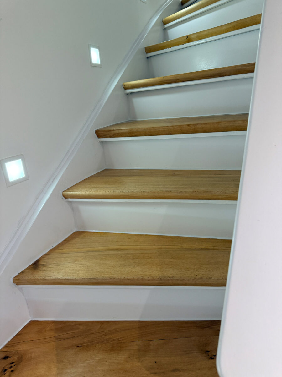 Eine moderne helle Holztreppe mit weißen Wänden und integrierten Quadratlampen