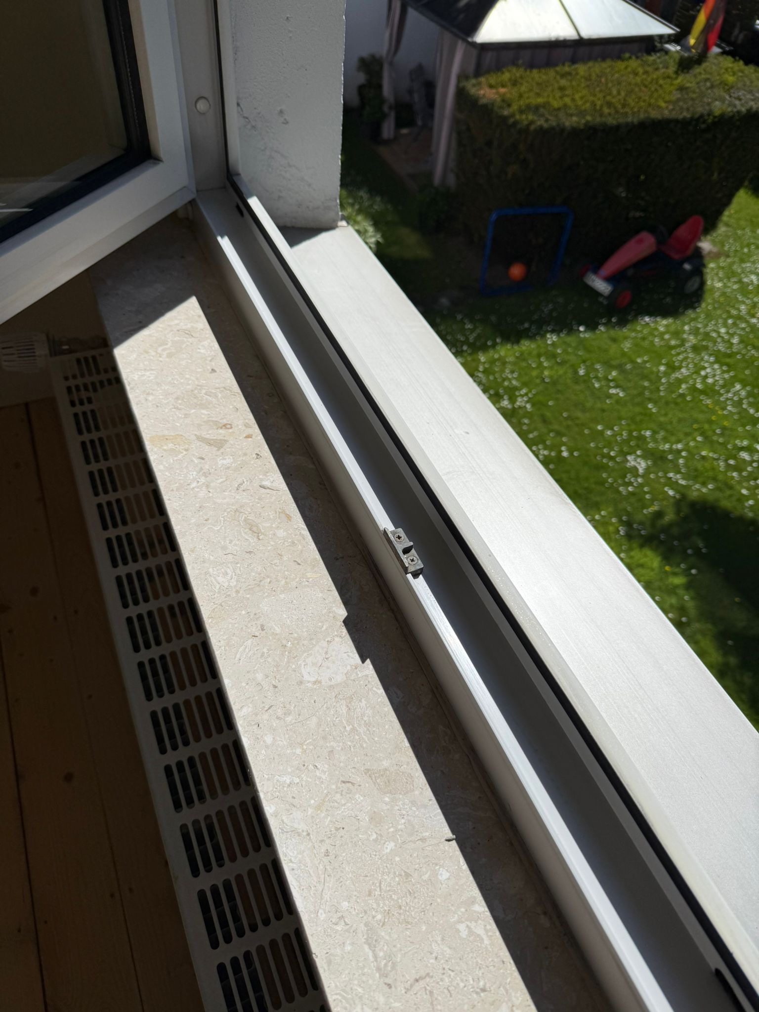 Offenes Fenster mit hellbeigem Fensterbrett, darunter Heizung, Blick auf grünen Garten