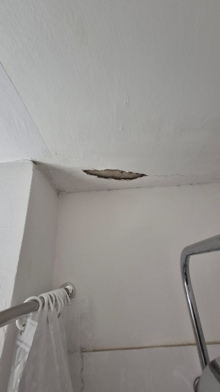 Eine weiße Zimmerdecke mit einem sichtbaren Loch zeigt abgeplatzten Putz